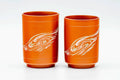 The two reddish-orange cups side by side, front view showing a white swirling design.