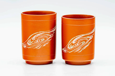 The two reddish-orange cups side by side, front view showing a white swirling design.
