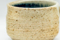 Close side view of the speckled beige exterior with a thin blue glaze line along the rim.