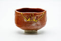 Orange-red raku matcha bowl with gold kintsugi repair lines, front view, rustic glaze with dark patches.
