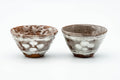 A pair of small yunomi cups in milky white glaze with rust speckles, set side by side.