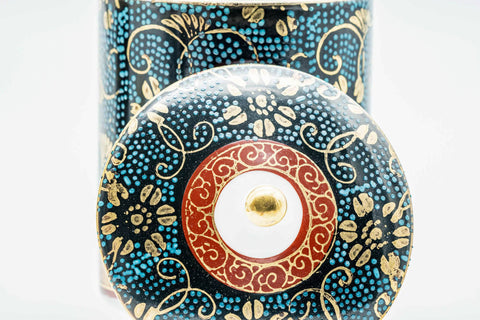 Close-up of a lid, showing the gold floral decoration and central knob.