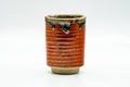 Speckled red yunomi teacup with a spiralling ribbed body, front view, with drip-glaze accents near the rim.