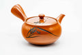 Red shudei Tokoname-yaki side-handle kyusu engraved with a long-grass design, lid on, three-quarter view.