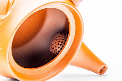 Close-up through the open teapot showing the fine ceramic mesh strainer inside.
