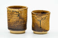 Pair of cylindrical teacups, one larger and one smaller, with brown-and-yellow drip glaze, shown side by side.