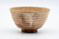 Loquat-coloured (biwa-iro) Hagi-yaki matcha bowl (chawan), three-quarter view showing the warm beige-orange glaze with soft vertical striations