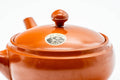 Three-quarter view showing the ceramic lid in place and a small maker's stamp impressed on the lower body.