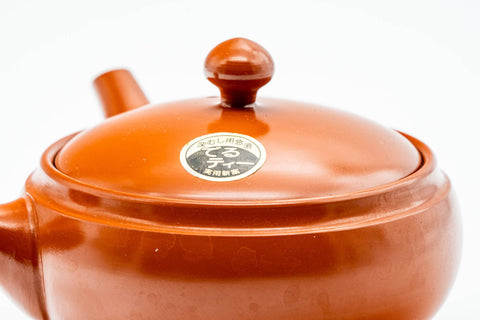 Three-quarter view showing the ceramic lid in place and a small maker's stamp impressed on the lower body.