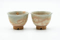 Front view of a matching pair of Hagi-yaki yunomi teacups with a dark beige glaze and pink gohonte spots, side by side.