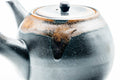 Three-quarter view highlighting the brown drip glaze flowing over the black body and lid.