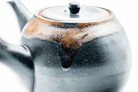 Three-quarter view highlighting the brown drip glaze flowing over the black body and lid.