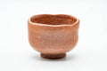 Pink-red raku wabi-sabi matcha bowl, front view, peachy mottled glaze on a hand-built body.