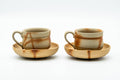 Pair of Bizen-yaki handled teacups, each resting on a matching saucer, front view, showing the reddish hidasuki straw-mark scorching.