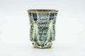 Tall flared yunomi teacup glazed in mottled grey-green and milky cream drip glaze, front view.