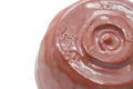 Close-up of the bowl's underside foot, showing the spiral mark in the red glaze.