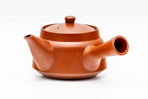 Teapot in profile showing the spout, side handle and unglazed brick-red clay