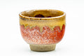 Close-up of a single cup showing the amber drip glaze over the red-orange body.