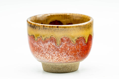 Close-up of a single cup showing the amber drip glaze over the red-orange body.