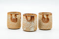 Orange Shino-glazed Mino-yaki yunomi shown upright from three angles, its white speckled glaze breaking over warm orange clay.