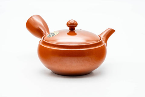 Side profile of the red clay teapot, spout to the left and hollow side handle facing the viewer.
