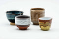 Set of four uniquely glazed guinomi teacups grouped together, showing teal, brown and speckled finishes, front view.
