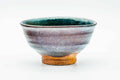 Front view of the chawan, glaze graduating from green-turquoise to earthy brown, resting on a pale foot.