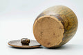 Open mizusashi lying on its side with the lid alongside, showing the small knob.