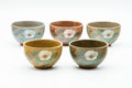 Set of five celadon-glazed yunomi cups in varied muted tones, each painted with a white camellia blossom.