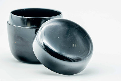 Small black-urushi ko-natsume matcha caddy, lid off, body upright with lid lying beside, three-quarter view of the interior