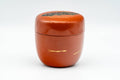 Japanese Natsume - Orange Gold Floral Lacquered Matcha Tea Caddy - 100ml - front three-quarter view of the closed caddy showing the orange urushi lacquer body and decorated lid