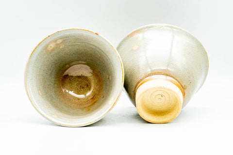 Two Hagi-yaki cups, one laid on its side showing the glazed interior with pooled glaze, the other upright revealing the unglazed foot.