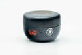 Black-lacquer floral matcha tea caddy, lid on, three-quarter view showing the red crest emblem on the body