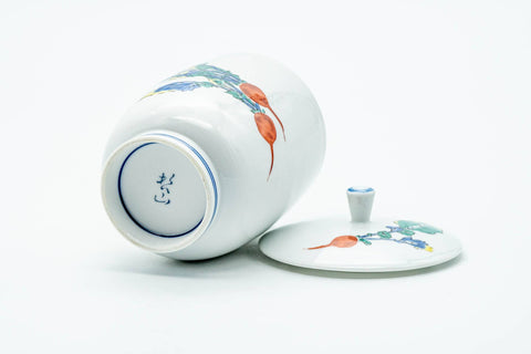 The cup tipped to show its footed base and stamp, lid resting alongside.