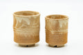 A pair of Hagi-yaki meoto yunomi with an engraved bamboo motif in a pale beige glaze, set side by side.
