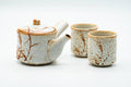 Cream Shino-glazed Mino-yaki tea set shown from the front, with a side-handled kyusu teapot and two matching yunomi teacups decorated with rust-orange brushwork.