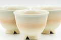 Low-angle view of the four Hagi teacups showing the peach-beige glaze gradient