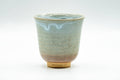 Hagi-yaki yunomi from the Tsubaki kiln, front view, pale beige-white glaze with a soft blue drip down the front and an exposed clay foot.