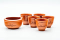 Red shudei Tokoname-yaki tea set shown from above: a spouted katakuchi water cooler surrounded by five small guinomi cups on a white background.