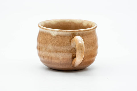 Three-quarter view of the teacup showing the side handle and tan drip glaze.