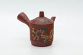Red shudei Tokoname kyusu with abstract green-and-gold nerikomi decoration, front three-quarter view with the spout to the left.