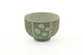 Floral and geometric Arita-yaki yunomi teacup, front view showing green chrysanthemum florals and a blue lattice band on white porcelain