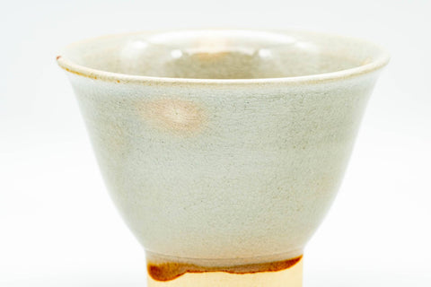 Close-up of a single beige Hagi-yaki cup, three-quarter view of the rim and softly streaked body.