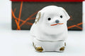 Front view of the seated white dog kogo with gold-accented features, in front of the box.