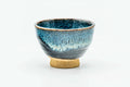 Single teal-blue drip-glazed guinomi teacup on a pale foot, front view.