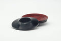 One saucer turned to reveal its matte black underside beside the red-lacquer stack.
