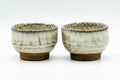 The two beige teacups standing side by side, front view, with a softly textured crackled glaze.