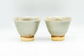 Pair of flared beige Hagi-yaki yunomi teacups side by side, front view with subtle hare's-fur streaking in the glaze.
