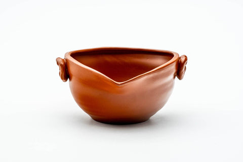 Three-quarter view showing the small wing handles on the side of the red clay bowl.