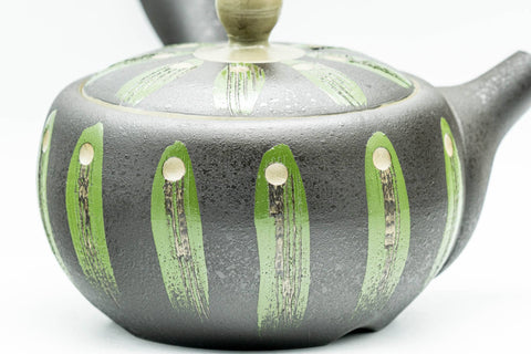 Close-up of the green geometric striped glaze on the teapot's black body.